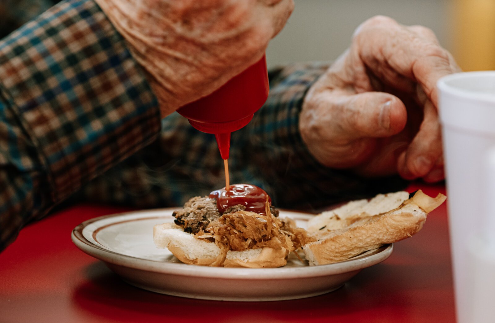 A customer puts ketchup on a hamburger slider.